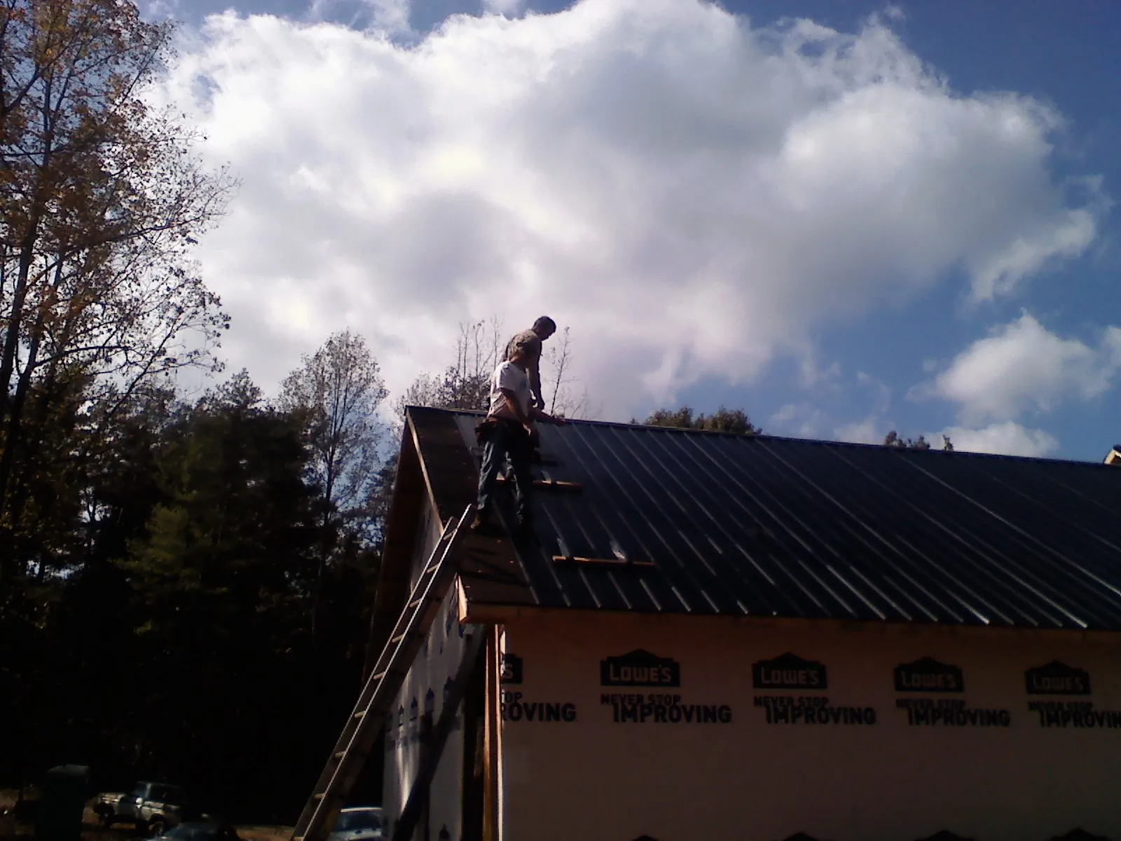 Roofer fastening dark metal panels high against a cloudy sky, from a Roof Inspection job in Stanwood